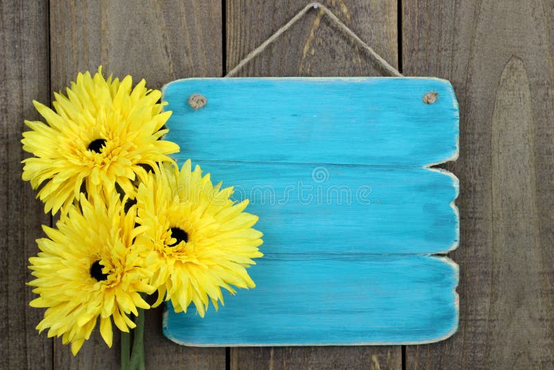Leeres antikes blaues Zeichen mit den großen gelben Sonnenblumen, die am rustikalen hölzernen Zaun hängen