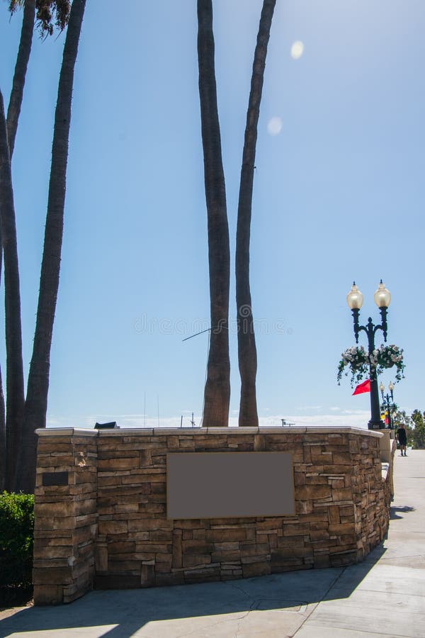 Leeres Zeichen gelegen durch eine Straße auf einer Steinwand mit Palmestämmen im Hintergrund stockfotografie Leeres Zeichen gelegen durch eine Straße auf einer Steinwand mit Palmestämmen im Hintergrund stockfotografie