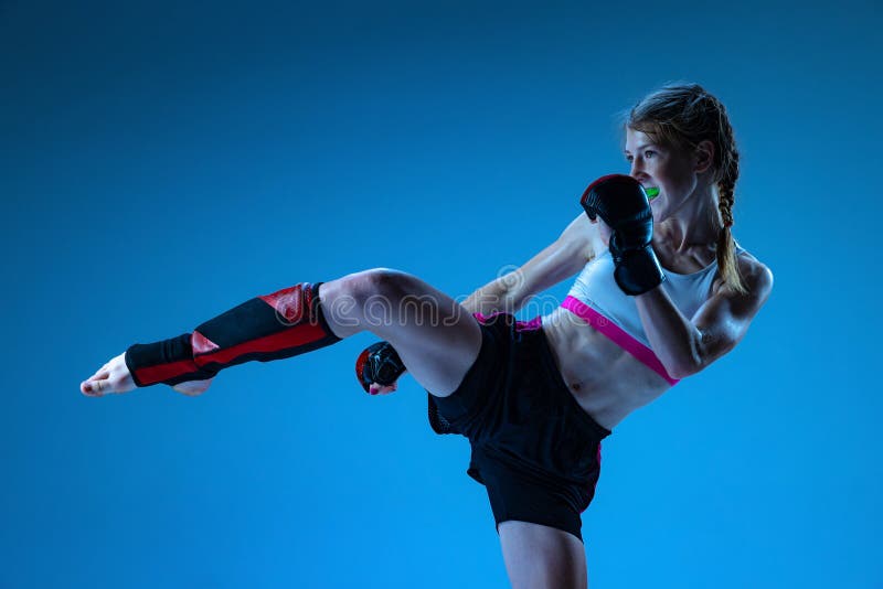 Studio shot of sportive teen-girl, MMA fighter in action, motion isolated on blue background in neon light. Concept of