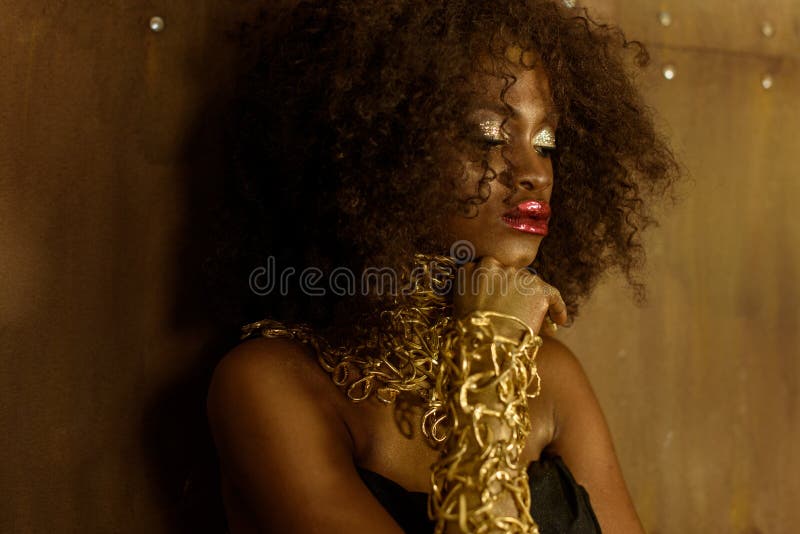 Leggen sloot de zijaanzicht Afrikaanse vrouw met gouden make-up en halsband, die handen op haar kinogen, de achtergrond van de br royalty-vrije stock afbeeldingen Leggen sloot de zijaanzicht Afrikaanse vrouw met gouden make-up en halsband, die handen op haar kinogen, de achtergrond van de br royalty-vrije stock afbeeldingen