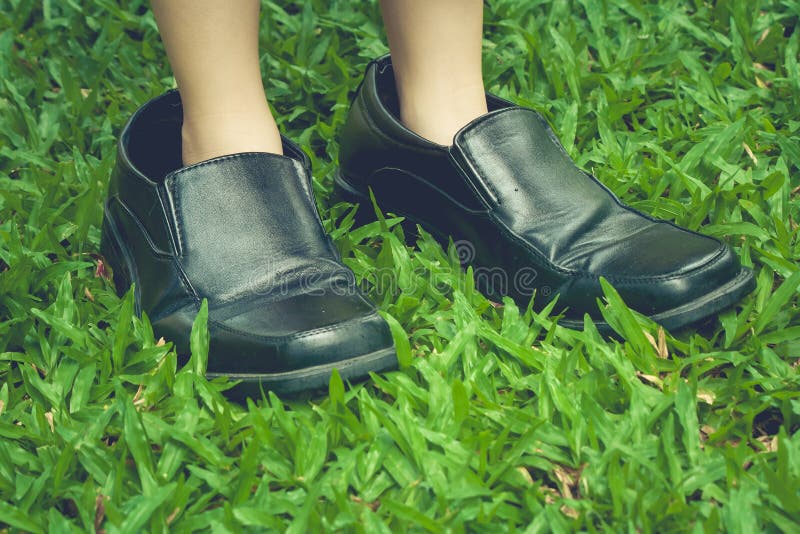 Legs of cute girl wearing black business shoes and standing on green grass.