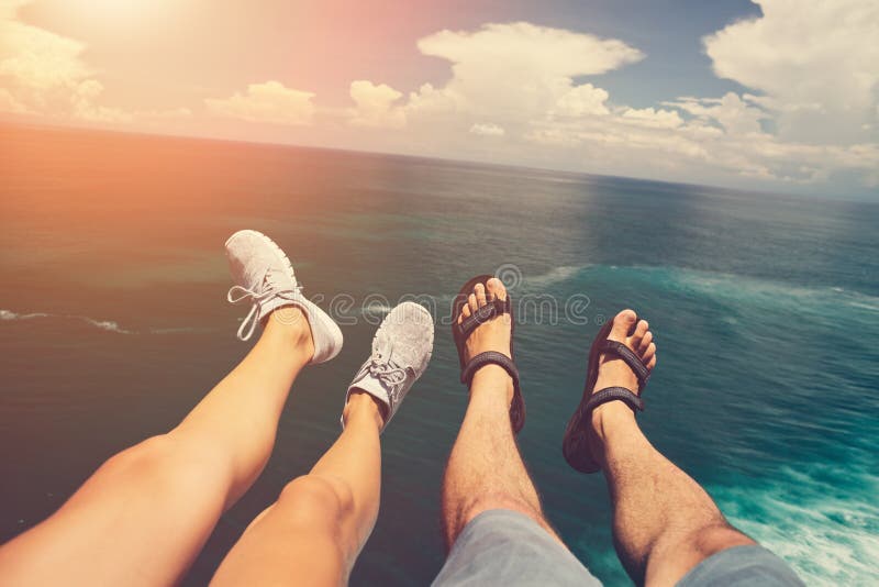 Legs of man in sandals and woman in sport shoes sitting above blue ocean stock photo Legs of man in sandals and woman in sport shoes sitting above blue ocean stock photo