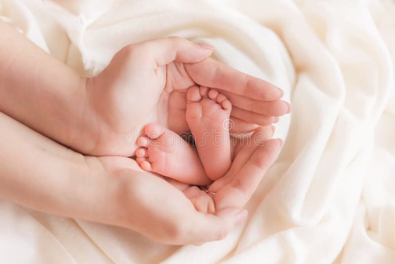 Legs of a newborn child in the palms of mother, mother`s day, mother`s universe