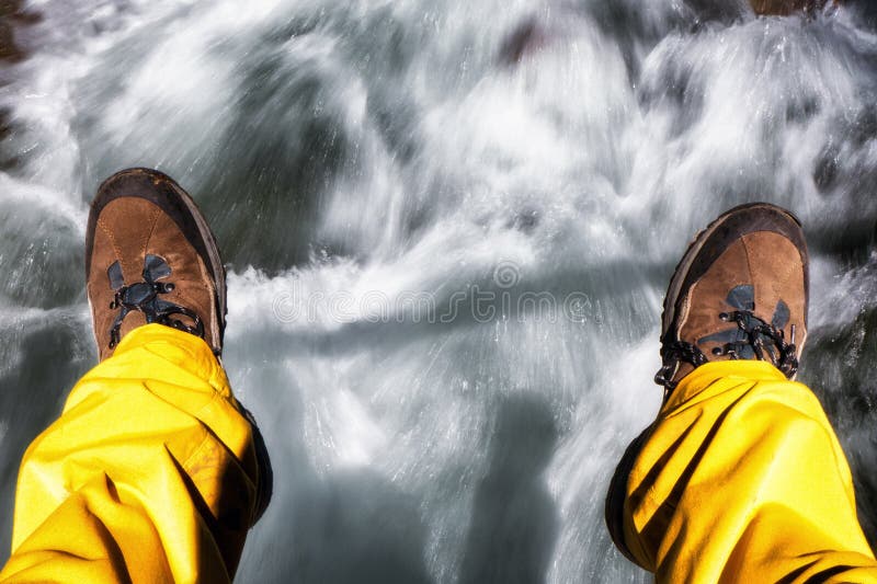 Legs og hiker with trekking boots over flowing water in mountain stream