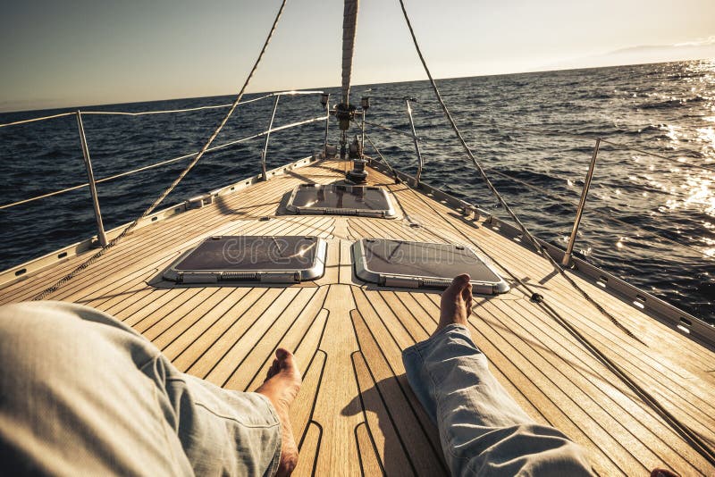 Legs point of view of man lay down enjoying the travel on a beautiful wooden sailboat with ocean around and un in front - concept