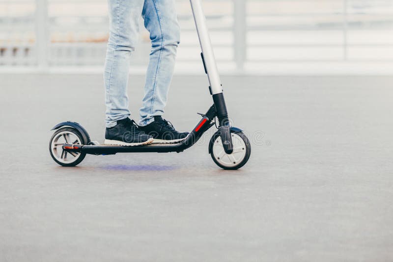Legs of unknown male in black sneakers and jeans rides on electric scooter over urban asphalt, enjoys sunny day. People and leisur stock image Legs of unknown male in black sneakers and jeans rides on electric scooter over urban asphalt, enjoys sunny day. People and leisur stock image
