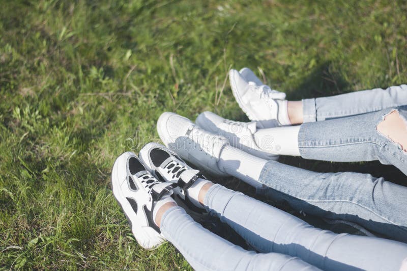 Legs of Young Girls. in Sneakers and Jeans. on the Grass. Stock Image ...