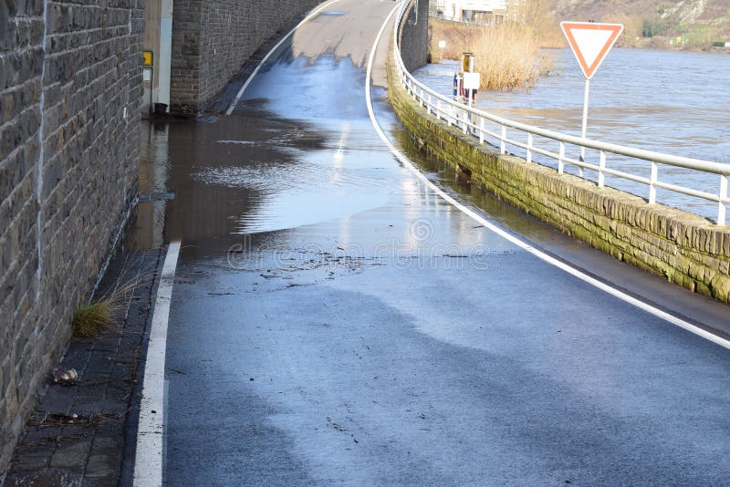 Mosel valley road near Lehmen during the winter flood with muddy water on the road intersection. A road maintenance truck is using a rotating brush on the ground to remove mud while the river Moselle is still bringing water back on the street. The brushed of muddy water goes back into the river flood, being on road level. It is a small winter flood. Mosel valley road near Lehmen during the winter flood with muddy water on the road intersection. A road maintenance truck is using a rotating brush on the ground to remove mud while the river Moselle is still bringing water back on the street. The brushed of muddy water goes back into the river flood, being on road level. It is a small winter flood