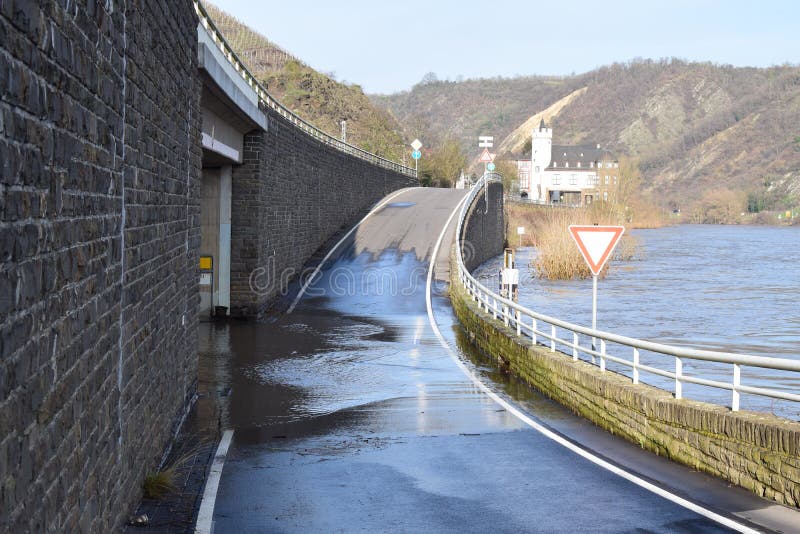 Mosel valley road near Lehmen during the winter flood with muddy water on the road intersection. A road maintenance truck is using a rotating brush on the ground to remove mud while the river Moselle is still bringing water back on the street. The brushed of muddy water goes back into the river flood, being on road level. It is a small winter flood. Mosel valley road near Lehmen during the winter flood with muddy water on the road intersection. A road maintenance truck is using a rotating brush on the ground to remove mud while the river Moselle is still bringing water back on the street. The brushed of muddy water goes back into the river flood, being on road level. It is a small winter flood