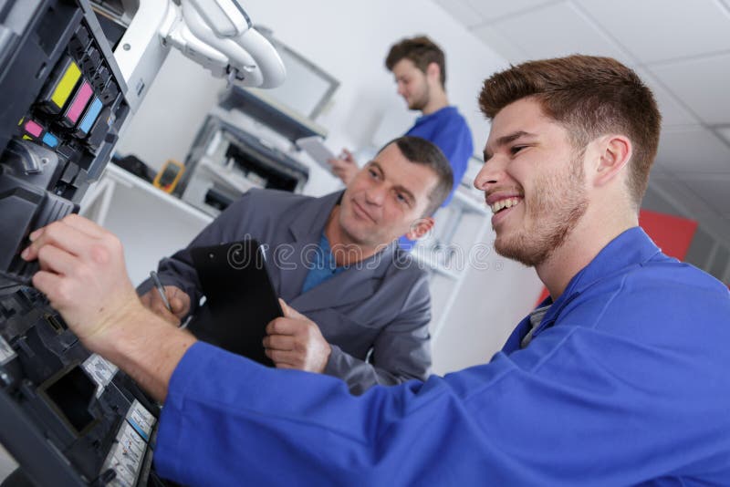 Apprentice repairing printer with teacher monitoring apprentice. Apprentice repairing printer with teacher monitoring apprentice