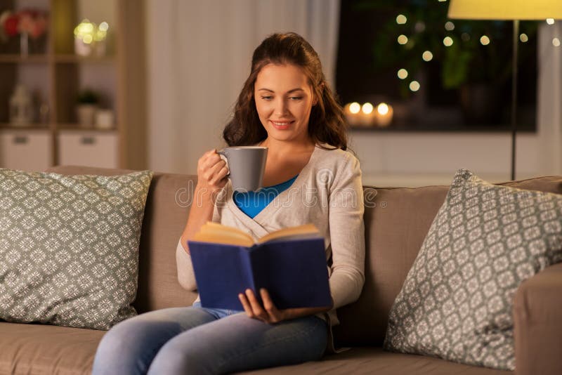 Young woman reading book at home in evening