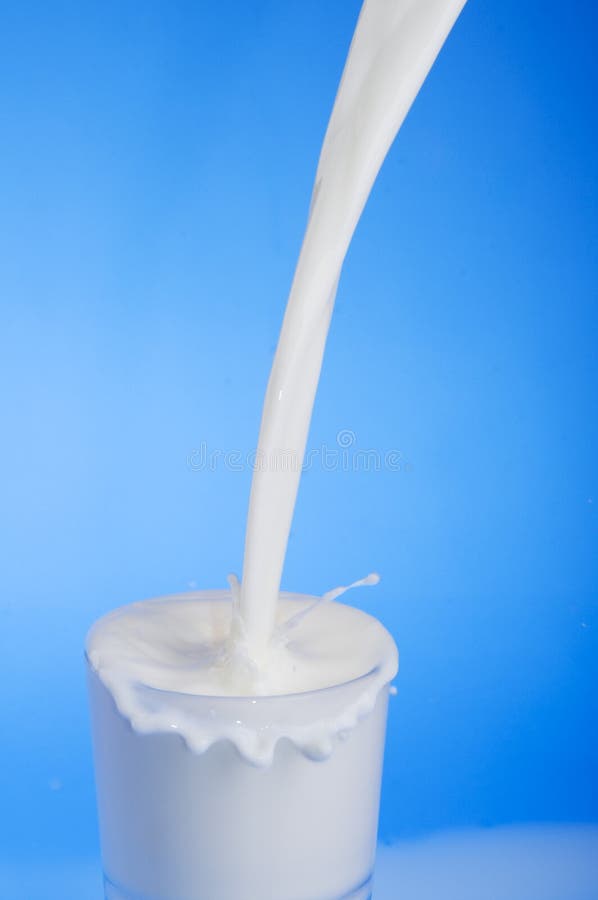 Stream of milk pouring into a glass over blue background. Stream of milk pouring into a glass over blue background