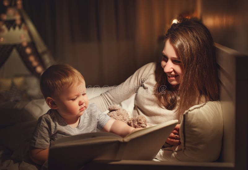 Leitura da família da noite as mães leem crianças livro antes do goin imagem de stock Leitura da família da noite as mães leem crianças livro antes do goin imagem de stock