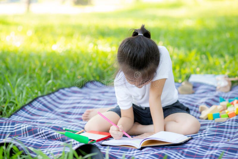 Leitura da menina e livro asiáticos pequenos novos da escrita no parque, nos trabalhos de casa da criança de Ásia e no estudo no fotografia de stock Leitura da menina e livro asiáticos pequenos novos da escrita no parque, nos trabalhos de casa da criança de Ásia e no estudo no fotografia de stock