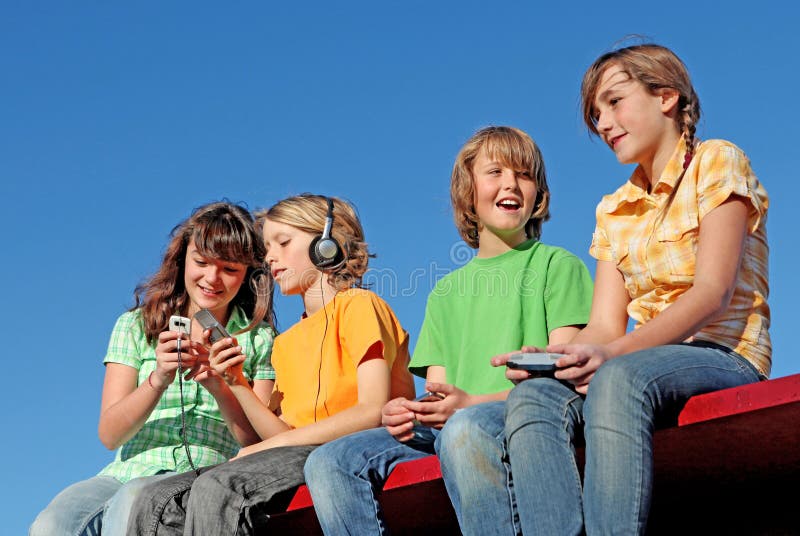 Group of happy kids or children playing with mobiles cell phones video games listening to music outdoors. Group of happy kids or children playing with mobiles cell phones video games listening to music outdoors