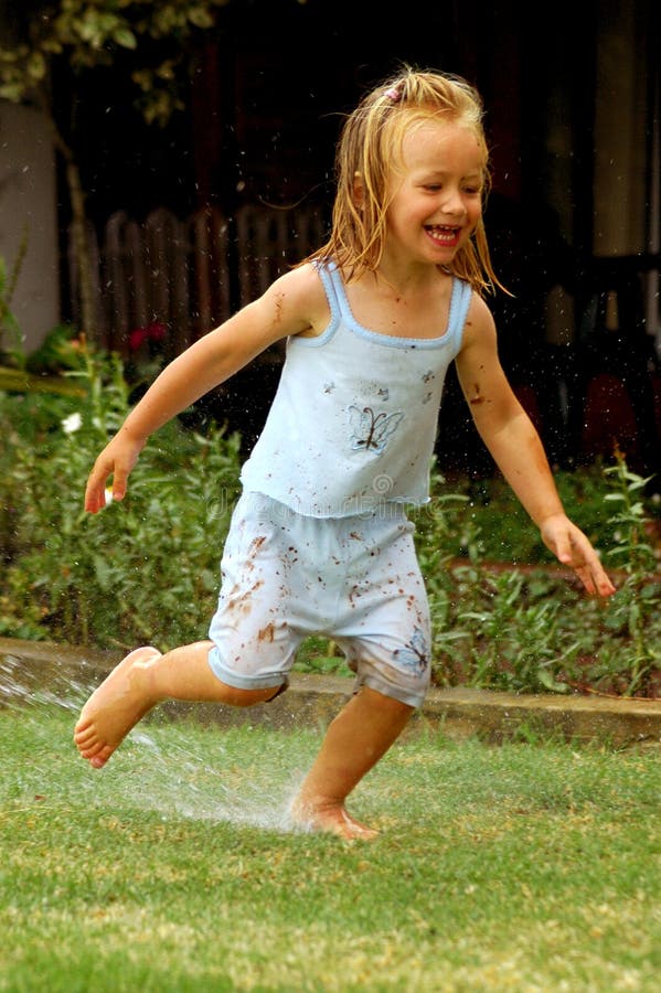 A little caucasian girl child with happy expression in the face running, playing and splashing with rain water having great fun in the garden outdoors in summer. A little caucasian girl child with happy expression in the face running, playing and splashing with rain water having great fun in the garden outdoors in summer