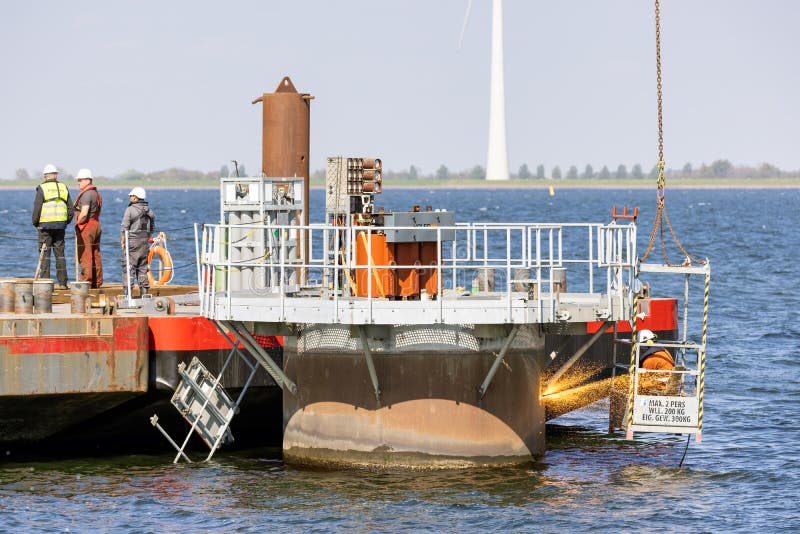 Lelystad, The Netherlands - April 22, 2022: Worker with cutting torch at work by demolition foundation offshore windturbine. Lelystad, The Netherlands - April 22, 2022: Worker with cutting torch at work by demolition foundation offshore windturbine