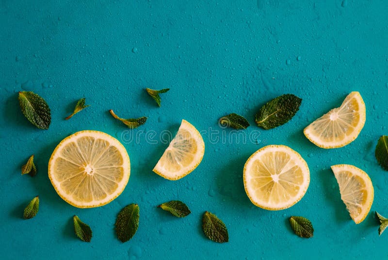 Lemon slices and mint herbs against blue background with copyspace. Top view of lemons and leaves