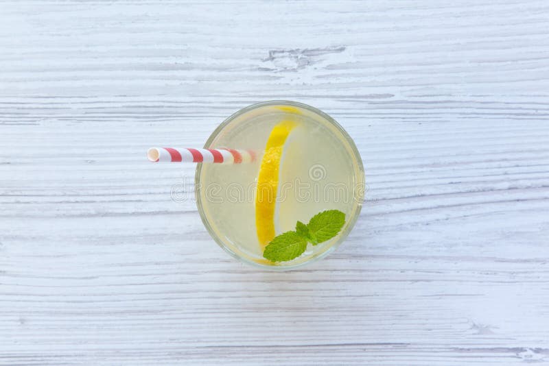 Lemonade drink in a glass with fresh lemon and mint over white wooden background, top view.