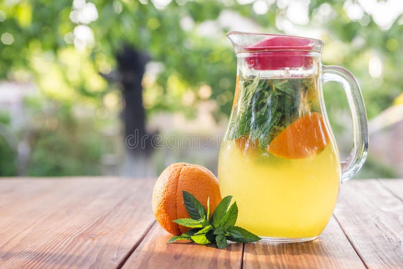 Lemonadkanna med apelsinen, mintkaramellen och is på trädgårdtabellen Hemlagad orange lemonad med mintkaramellen arkivfoton Lemonadkanna med apelsinen, mintkaramellen och is på trädgårdtabellen Hemlagad orange lemonad med mintkaramellen arkivfoton