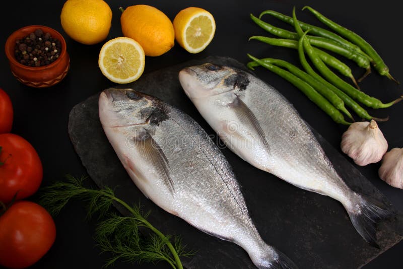 Lemons, tomatoes, hot peppers and two carcasses fresh raw atlantic saltwater fish Sparus aurata with shiny silver scales lie on a royalty free stock images Lemons, tomatoes, hot peppers and two carcasses fresh raw atlantic saltwater fish Sparus aurata with shiny silver scales lie on a royalty free stock images