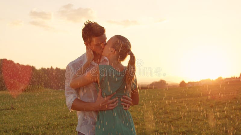 CLOSE UP: Cheerful young couple kisses in the rain during romantic outdoor date.