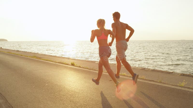 LENS FLARE: Unrecognizable jogging couple on holiday soaking up the sun rays. royalty free stock photos