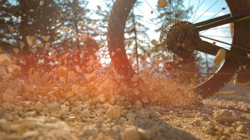 LENS FLARE: Unrecognizable man brakes while riding a bike down gravel track. royalty free stock image