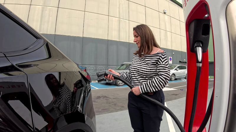 Lentement de la femme hispanique mettant la fiche dans sa voiture électrique pour la charger dans la station. banque de vidéos
