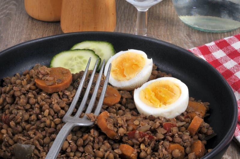 Lenticchie con fette di cetriolo di carote e uova sode servite su un piatto con chiusura di forchetta. Chiudere un piatto di verdure cotte servito alla tavola con anelli d'uovo sodi alette