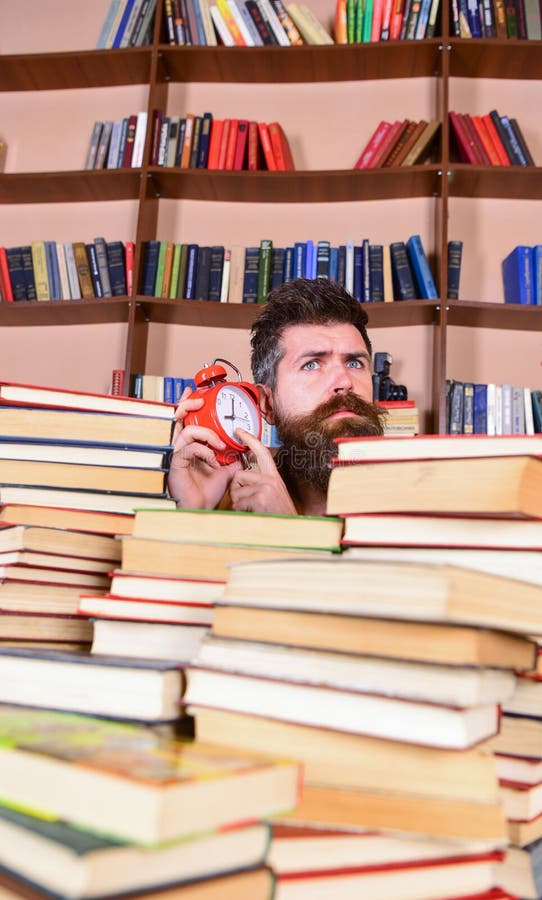 Leraar of student die met baard in bibliotheek bestuderen Mens, wetenschapper die uit stapels van boeken met wekker gluren Mens royalty-vrije stock foto's Leraar of student die met baard in bibliotheek bestuderen Mens, wetenschapper die uit stapels van boeken met wekker gluren Mens royalty-vrije stock foto's