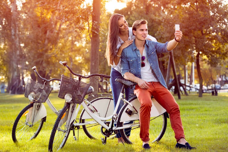 Les ajouter de sourire aux bicyclettes et au smartphone en automne se garent image libre de droits Les ajouter de sourire aux bicyclettes et au smartphone en automne se garent image libre de droits