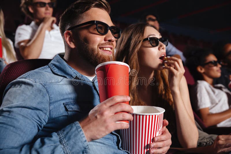 Image of loving couple friends sitting in cinema watch film eating popcorn and drinking aerated sweet water. Image of loving couple friends sitting in cinema watch film eating popcorn and drinking aerated sweet water.