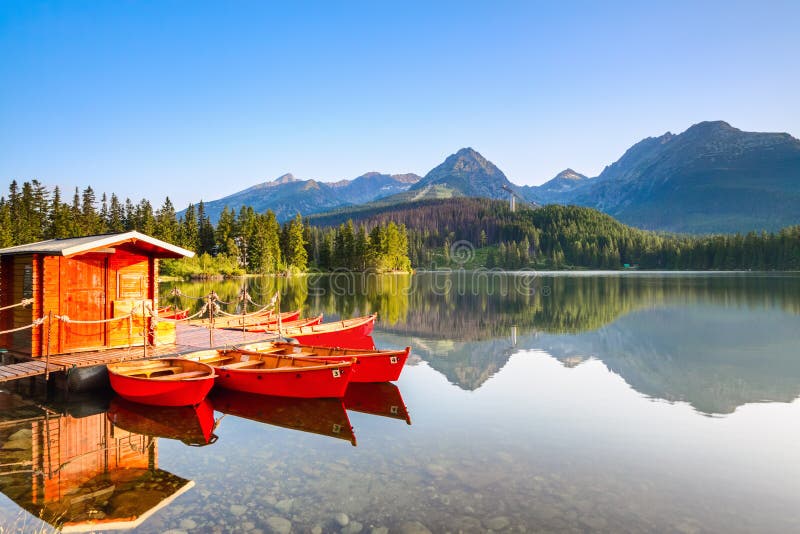 Red boats moored at wooden house on a lake with a clear water against the background of high mountains.Strbske Pleso lake, Slovakia, Tatra mountains. Red boats moored at wooden house on a lake with a clear water against the background of high mountains.Strbske Pleso lake, Slovakia, Tatra mountains.