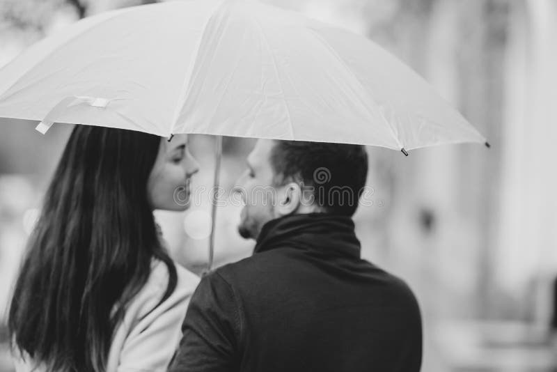 Les beaux couples, le type et son amie habill?s dans des v?tements sport se tiennent sous le parapluie et regardent l'un l'autre image stock Les beaux couples, le type et son amie habill?s dans des v?tements sport se tiennent sous le parapluie et regardent l'un l'autre image stock