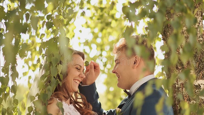 Les beaux et heureux jeunes mariés sous les branches des arbres de bouleau se réjouissent ensemble