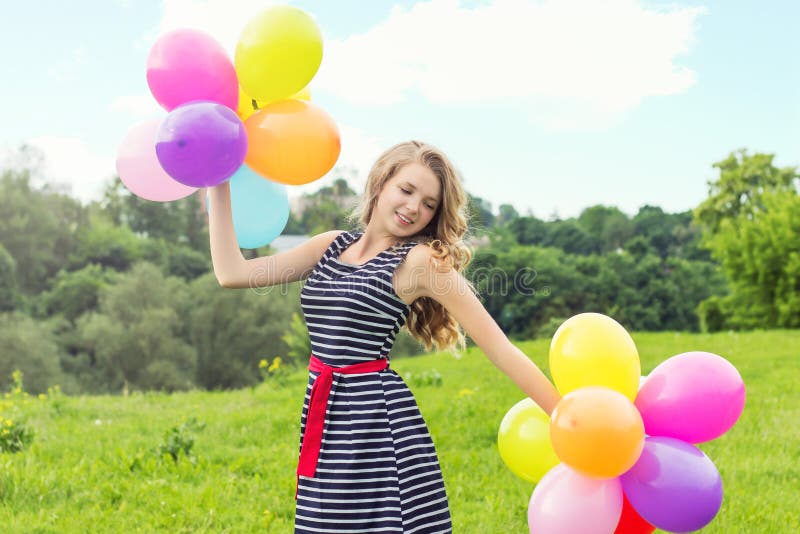 Les beaux jeunes sourires blonds de fille un jour d'été marche avec les boules colorées dans la ville images stock