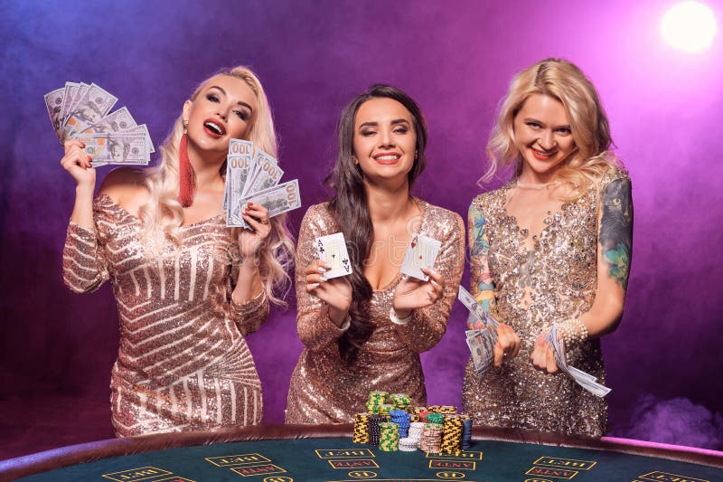 Les belles filles avec des coiffures parfaites et maquillage lumineux posent la position à une table de jeu Casino, tisonnier photos stock Les belles filles avec des coiffures parfaites et maquillage lumineux posent la position à une table de jeu Casino, tisonnier photos stock
