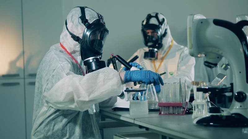 Les citoyens des tenues de protection travaillent avec des microscopes dans le laboratoire pendant la pandémie du syndrome respira