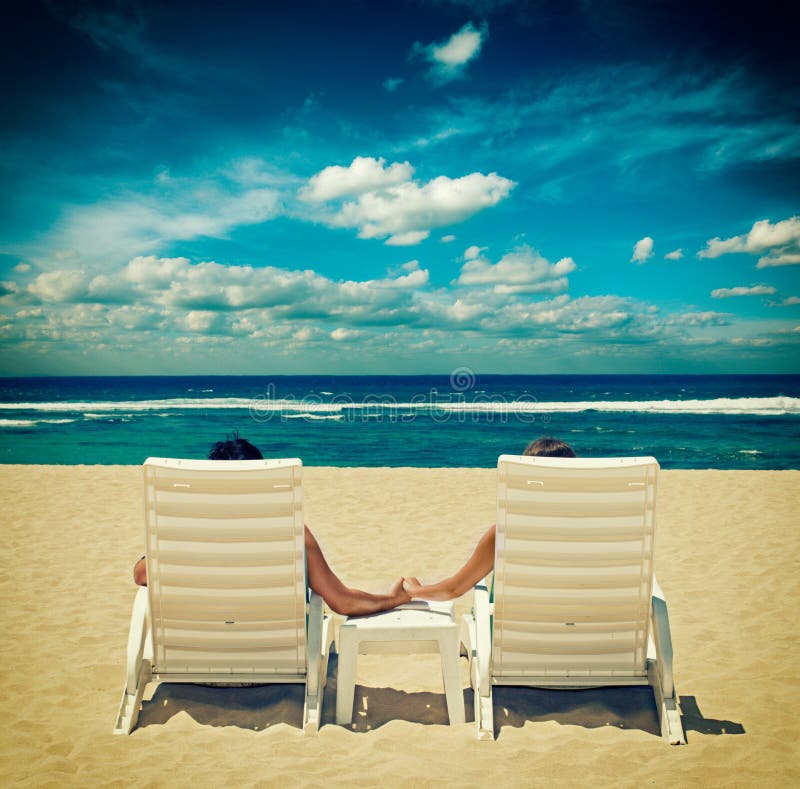 Les couples dans des chaises de plage tenant des mains s'approchent de l'océan photographie stock Les couples dans des chaises de plage tenant des mains s'approchent de l'océan photographie stock