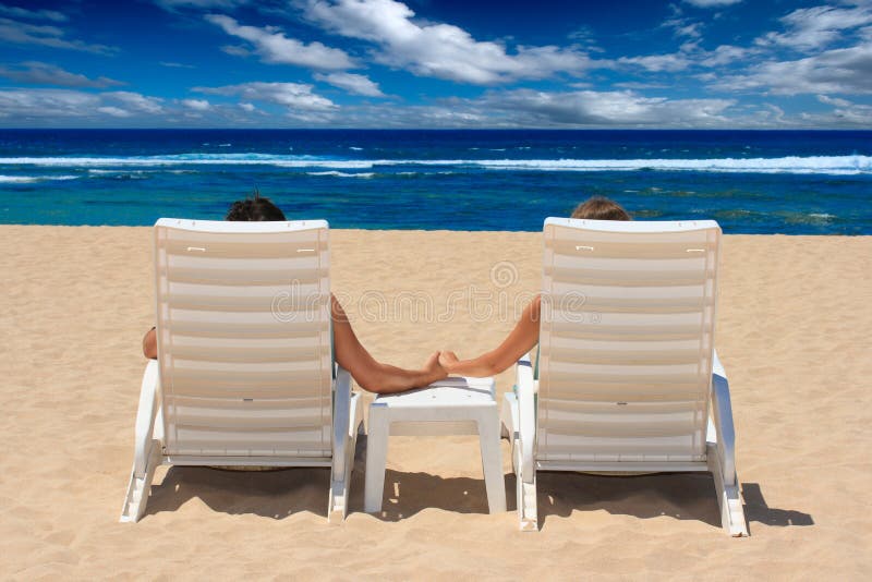 Les couples dans des présidences de plage retenant des mains s'approchent de l'océan photographie stock Les couples dans des présidences de plage retenant des mains s'approchent de l'océan photographie stock