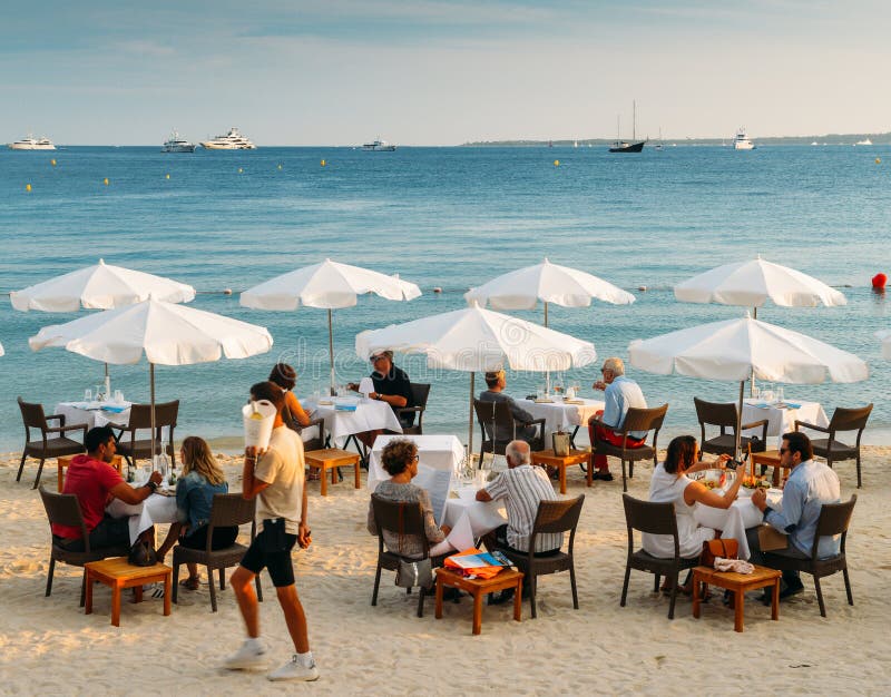 Juan les Pins, France - July 7th, 2018: Couples have drinks and appetizers at a luxurious restaurant on the beach in the French Riviera resort town of Juan les Pins, Cote d`Azur, France. Juan les Pins, France - July 7th, 2018: Couples have drinks and appetizers at a luxurious restaurant on the beach in the French Riviera resort town of Juan les Pins, Cote d`Azur, France