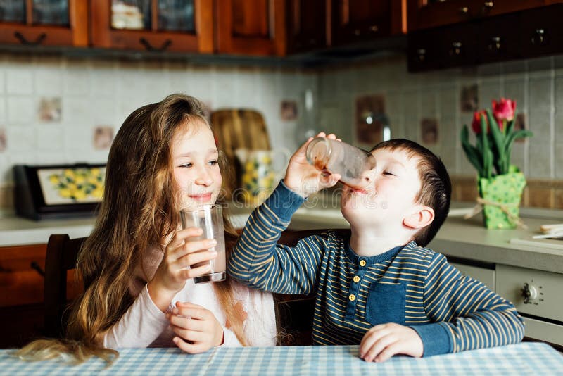 Les enfants boivent du lait dans la cuisine au matin La soeur et le frère préparent le cacao photographie stock Les enfants boivent du lait dans la cuisine au matin La soeur et le frère préparent le cacao photographie stock