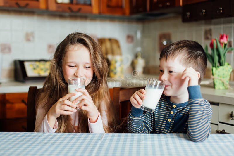 Les enfants boivent du lait et ont l'amusement dans la cuisine au matin photographie stock Les enfants boivent du lait et ont l'amusement dans la cuisine au matin photographie stock