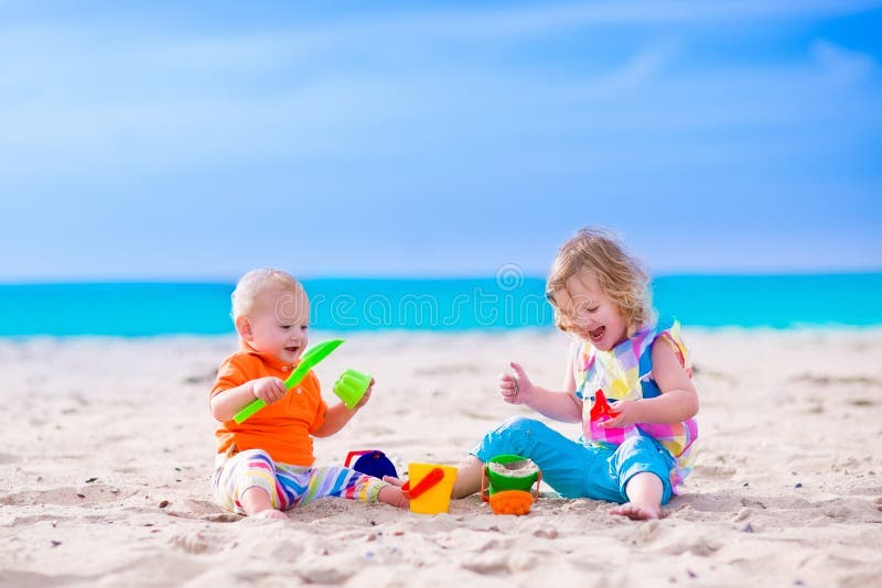 Kids play on a beach. Children building sand castle on tropical island. Summer water fun for family. Boy and girl with toy buckets and spade at the sea shore. Ocean vacation with baby and toddler kid. Kids play on a beach. Children building sand castle on tropical island. Summer water fun for family. Boy and girl with toy buckets and spade at the sea shore. Ocean vacation with baby and toddler kid.