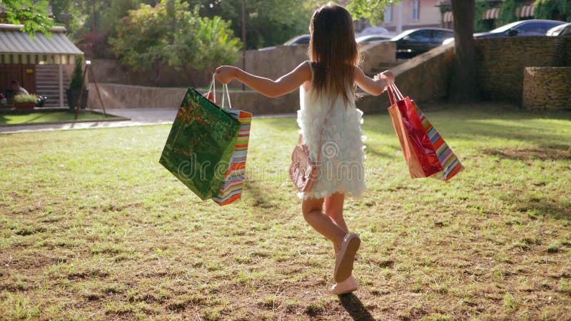 Les enfants faisant des emplettes, petite fille saute avec beaucoup de paquets dans des mains après des achats dehors banque de vidéos Les enfants faisant des emplettes, petite fille saute avec beaucoup de paquets dans des mains après des achats dehors banque de vidéos