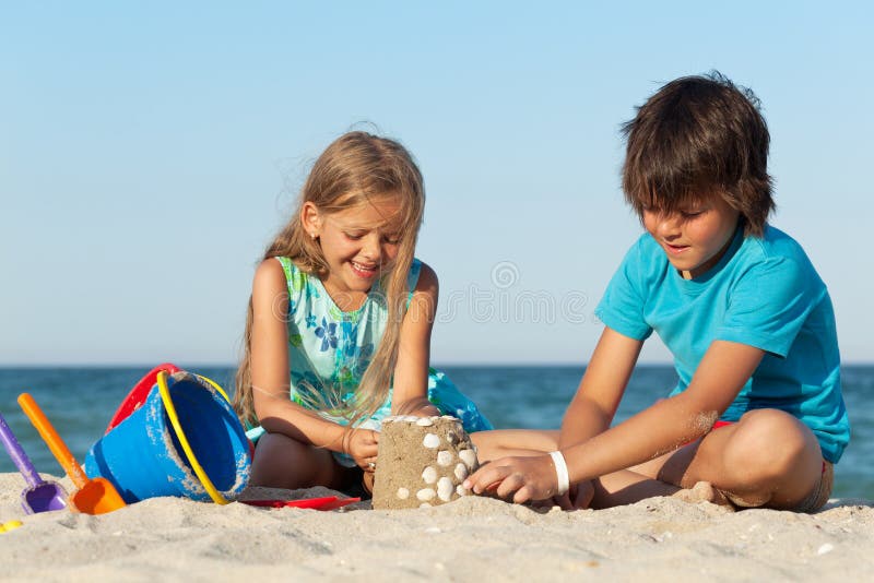 Kids playing on the beach building a sand castle decorating it with seashells. Kids playing on the beach building a sand castle decorating it with seashells