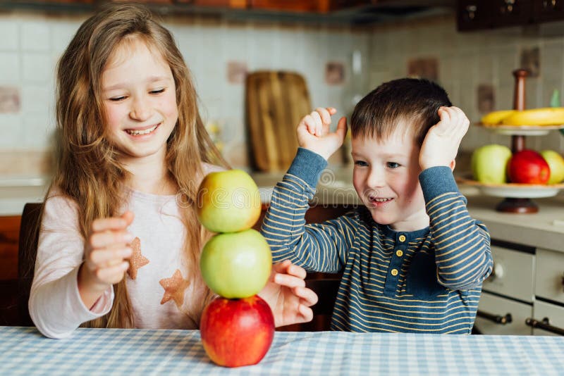 Les enfants mangent des pommes et ont l'amusement dans la cuisine au matin photographie stock libre de droits Les enfants mangent des pommes et ont l'amusement dans la cuisine au matin photographie stock libre de droits