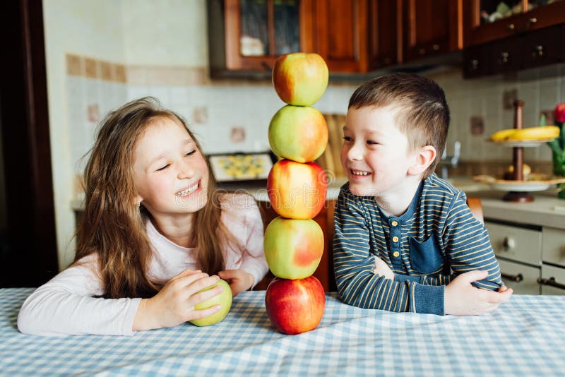 Les enfants mangent des pommes et ont l'amusement dans la cuisine au matin images libres de droits Les enfants mangent des pommes et ont l'amusement dans la cuisine au matin images libres de droits