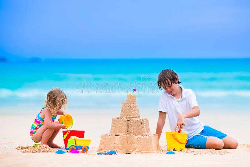 Kids playing on a beach. Two children build a sand castle at the sea shore. Family vacation on a tropical island. Boy and girl digging with toy spade and kid spade. Traveling with young child. Kids playing on a beach. Two children build a sand castle at the sea shore. Family vacation on a tropical island. Boy and girl digging with toy spade and kid spade. Traveling with young child.